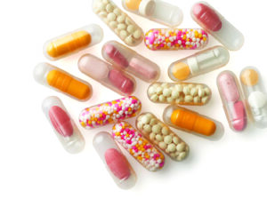 Farmaceutske kapsle punjenje supstancama različitih boja. Providne farmaceutske kapsule punjenje farmaceutskim granulama bele boje, prahm narandžaste boje, granulama crvene i bele boje, tabeltana roze boje.