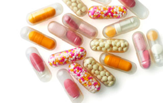 Farmaceutske kapsle punjenje supstancama različitih boja. Providne farmaceutske kapsule punjenje farmaceutskim granulama bele boje, prahm narandžaste boje, granulama crvene i bele boje, tabeltana roze boje.