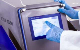 Ekran Mettler Toledo metal detektora i ruka operatera koja pririska opcijua na touch screen ekranu.